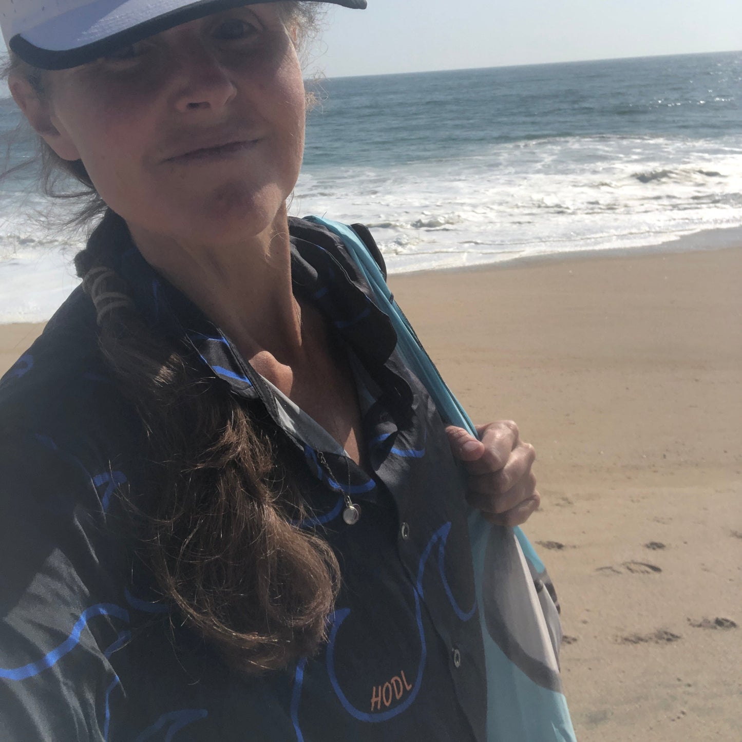 Person holding a surfboard on a beach with ocean in the background
